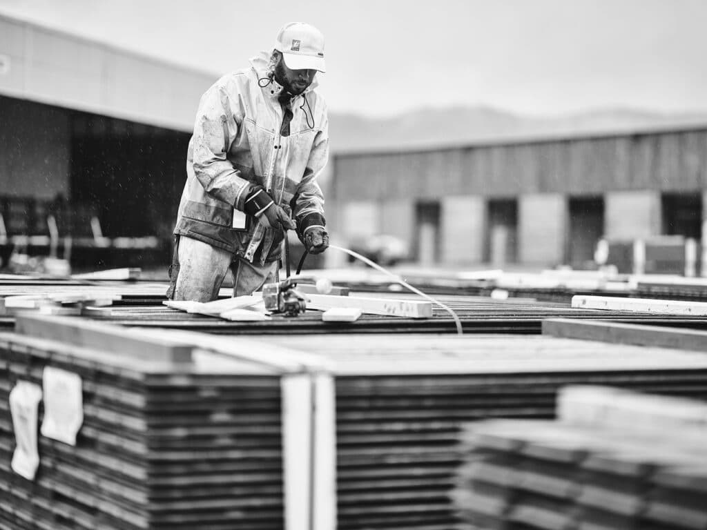 Miljøfoto fra produksjonen hos Talgø. Ansatt som stropper fast materialer før transport. Svart/Hvitt.